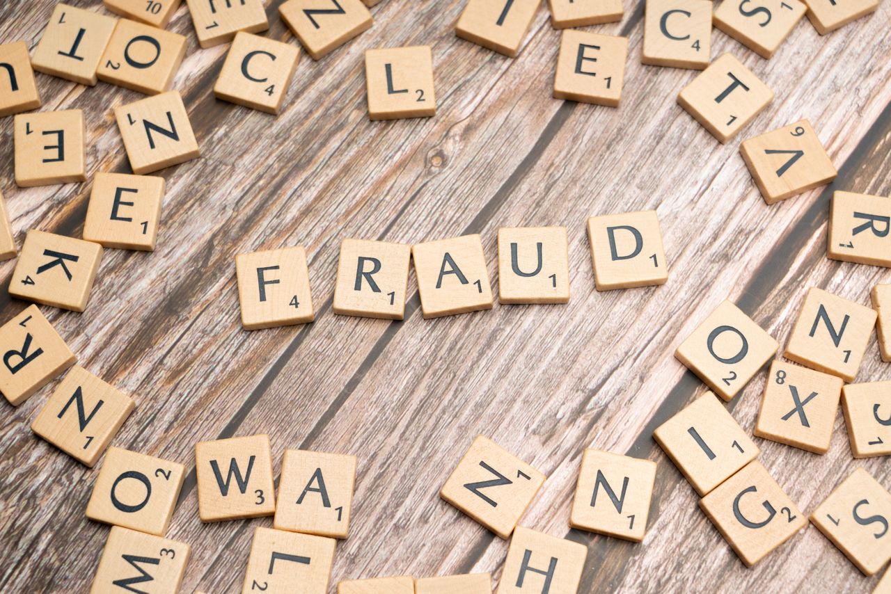 home-hero-bg Alphabet tiles arranged to spell fraud on a wooden surface, symbolizing deception.