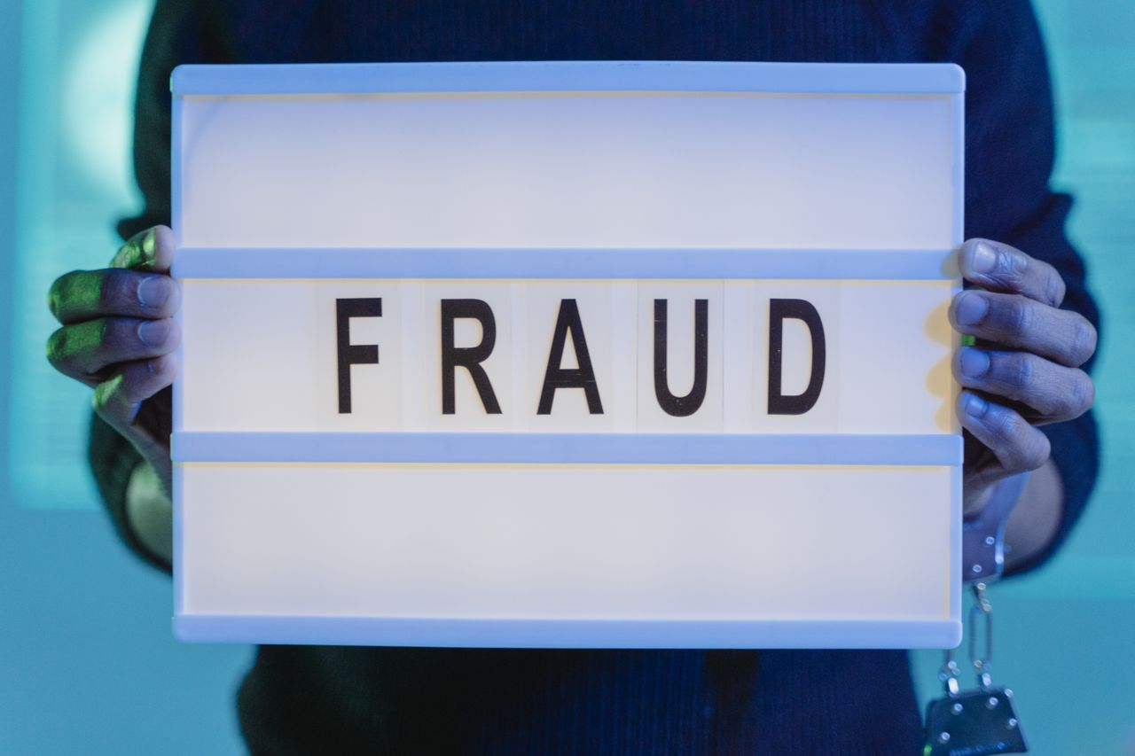 about-01 Close-up of hands holding a sign with fraud, illuminated in blue light.